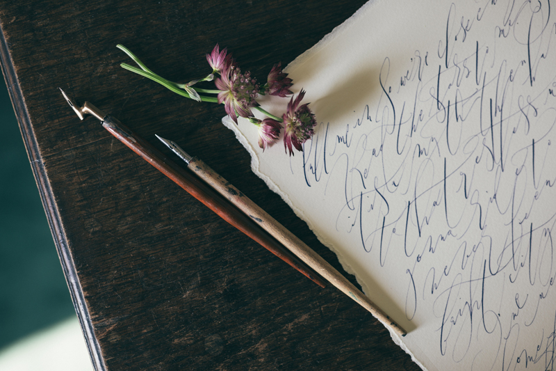 messy modern calligraphy on a desk with ink-stained pens and a few autumn flower stems