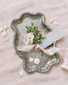 Grey name tag with hand calligraphy in white ink and a pretty flower buttonhole on a silver tray