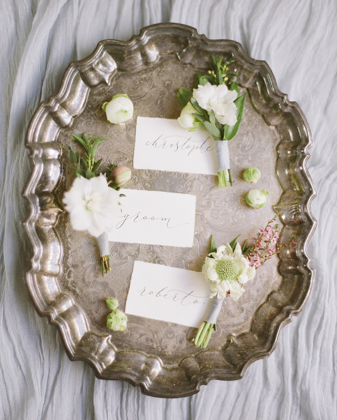 simple and elegant calligraphy wedding place names on a silver tray with flowers scattered around them