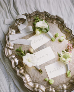 Silver tray of wedding place names in calligraphy with floral buttonholes for a wedding
