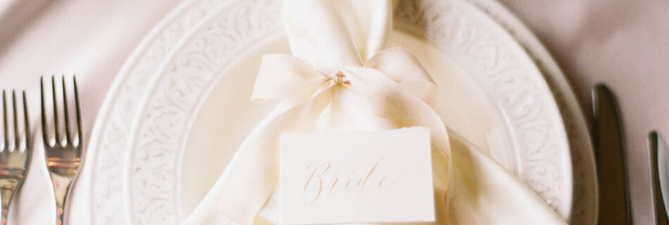Elegant modern wedding styling with white plates and an ivory napkin which has a calligraphy place name balanced on top