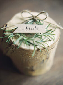 wedding name pennant style place card with 'bride' in calligraphy on a rosemary sprig and log slice