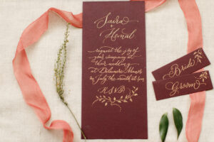 Wedding invitation in relaxed modern calligraphy using gold ink on burgundy slimline card