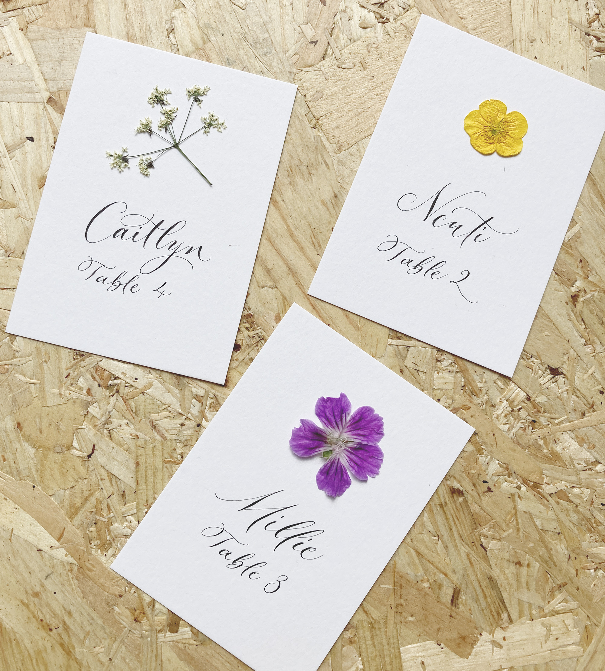 Wedding place names with pressed flowers: cow parsley, buttercup and geranium
