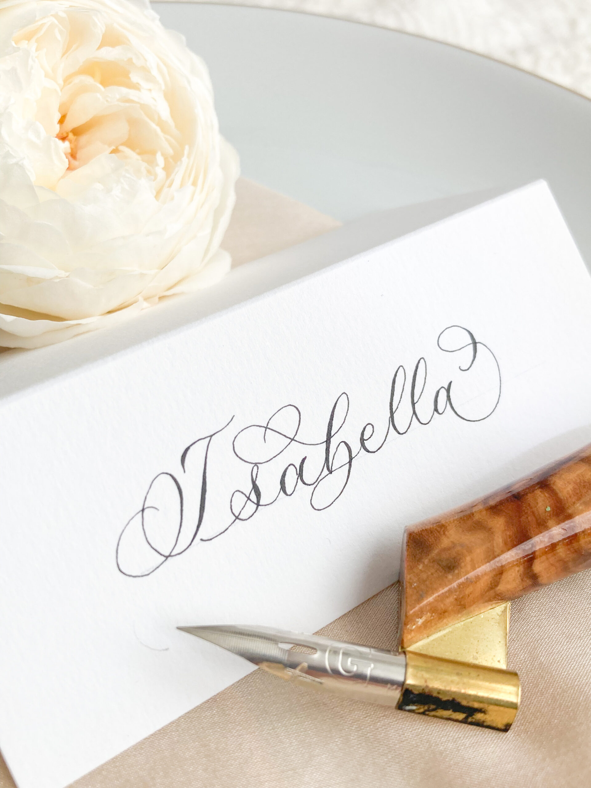 high quality wedding calligraphy place name with a polished wooden penholder and metal nib, next to a rose