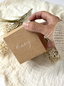 hand picking up a small Kraft box with white calligraphy lettering
